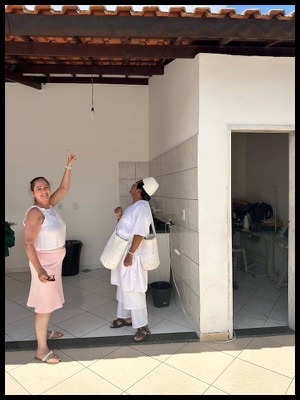 06-Feira-de-Santana-Vewnerable-Mamo-Arwa-Viku-Pagamentos-Isabel indicando aonde aconteceu o furo no telhado pelo projétil que furou também o chão.  Segundo Isabel, esse quarto dos fundos era maior